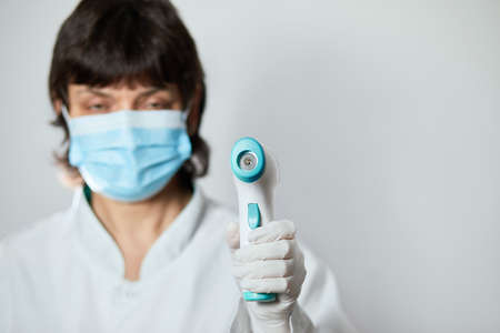 Doctor wearing protective mask ready to use infrared forehead thermometer to check body temperature for virus symptoms - epidemic virus outbreak concept. Coronavirus.Thermometer gunの写真素材