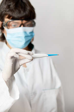 Doctor looking at thermometer. Female hands holding a digital thermometer. Girl measures the temperature. Check body temperature for virus symptoms flu, epidemic coronavirusの写真素材
