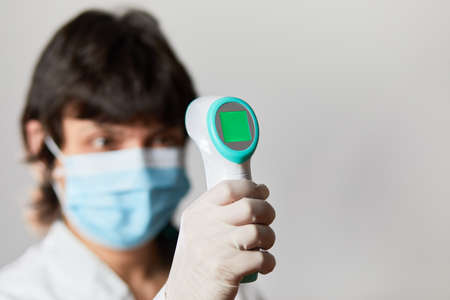 Doctor wearing protective mask ready to use infrared forehead thermometer to check body temperature for virus symptoms - epidemic virus outbreak concept. Coronavirus.Thermometer gunの写真素材