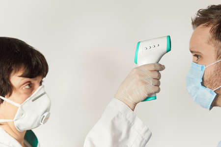 Doctor wearing a respirator N95 mask to use infrared forehead thermometer to check body temperature for virus symptoms. Respiratory diseases such as flu, coronavirus. Epidemic outbreakの写真素材