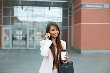 Business Woman With Phone Near Office. Portrait Of Beautiful Smiling Female Talking On Phone While Standing Outdoors. Phone Communication.の写真素材