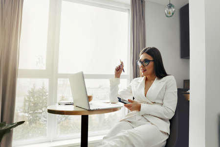 Beautiful happy woman using mobile phone while working at home with laptop. Smiling woman wearing eyeglasses messaging with smartphone.の写真素材