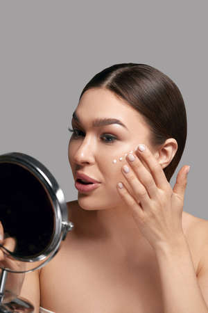 Skin care. Woman with beauty face touching healthy facial skin portrait. Beautiful smiling girl model looking on mirrorの写真素材