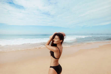 Portrait of pretty beautiful fashion woman in black bikini posing in summer near the sea and blue sky. Young Girl with tanned sexy body in swimwear with copy space. Summer lifestyle. Vacationの写真素材