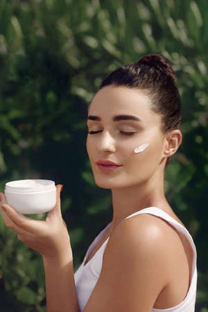 beauty concept. Beautiful Woman Model With Moisturizing Cream On Face. Portrait of Girl in Tropical Leaves. Body And Skin care.の写真素材