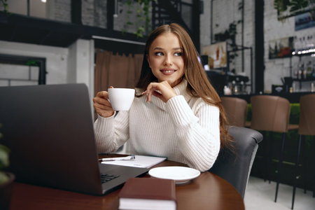 Beautiful woman in a cafe drinking coffee and smiling. Girl holds cup of cappuccino.の写真素材