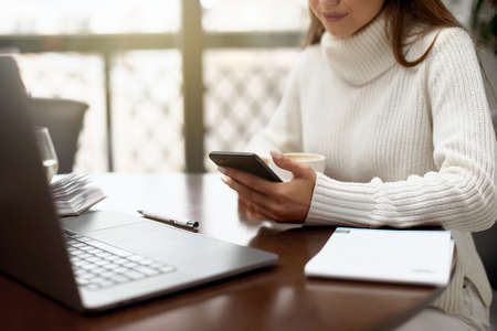 Woman using phone and drinking coffee in a cafeの写真素材