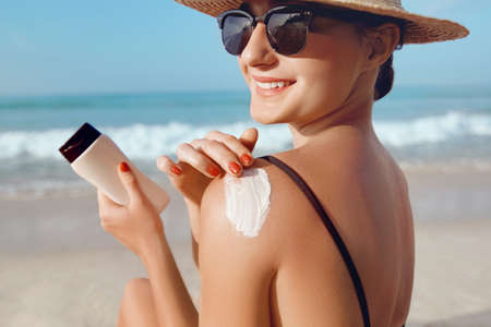 Girl Using Sunscreen to Skin. Beautiful Woman in Bikini Applying Sun Cream on Tanned Shoulder. sun protection. Skin and Body Care.の写真素材