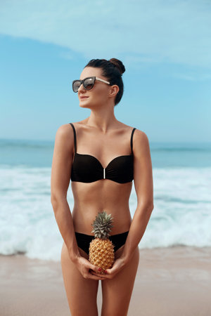 Beautiful Woman with bronze tan in bikini holds pineapples in handsの写真素材