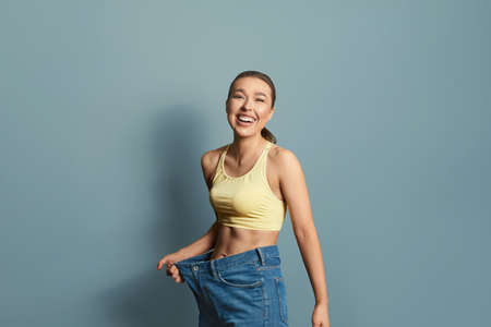 Happy woman after weight-loss is try her old jeans. Isolated on blue backgroundの素材 [FY310184490057]