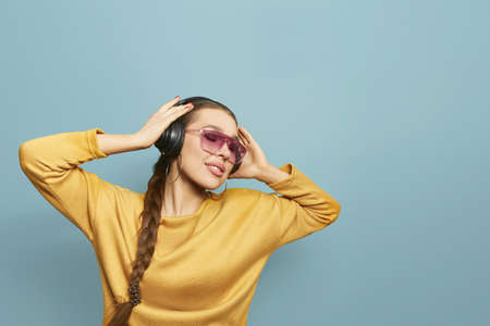 Beautiful woman with sunglasses in yellow sweater listening to music with wireless headphones. Girl uses wireless earphones and dancing.の写真素材