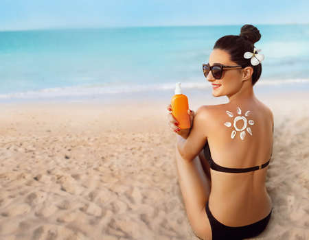 skincare. sun protection. Woman apply sun cream. Woman With Suntan Lotion On Beach In Form Of The Sun. Portrait Of Female With Drawn Sun On A Shoulder. Suncream. Girl Holding Moisturizing Sunblock.の写真素材