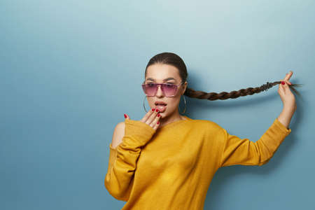 Portrait of a excited young beautiful woman with sunglasses holding to the hair. isolated blue backgroundの写真素材