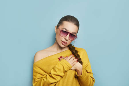 Lovely young woman presses palms to heart, feels touched and grateful, dressed in yellow jumper, isolated over blue backgroundの写真素材