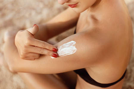 Girl Using Sunscreen to Her Skin. Woman Applying Sun Cream on Tanned Shoulder. sun protection. Skin...