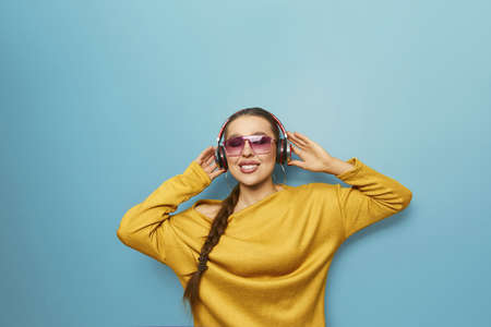 Young woman on blue background listening to music with wireless headphones. Girl using phone of listening to music with wireless earphones.の写真素材