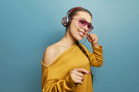 Young woman dancing while listening to music with headphones isolated over blue background