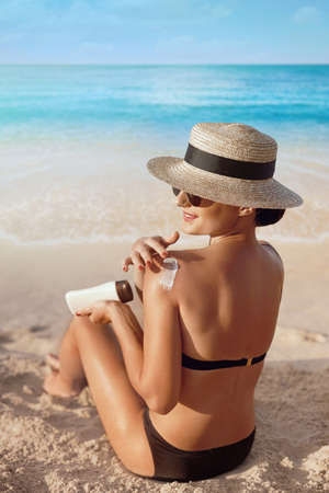 Woman apply sun cream on her tanned Shoulder. beautiful girl on the beach.の写真素材