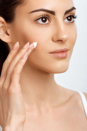 facial care. Female Applying Cream.Portrait Of Young Woman With Cosmetic Cream On Skin. Closeup Of Beautiful Girl With Beauty Product On Soft Skin, Natural Makeup Touching Face. high resolutionの写真素材