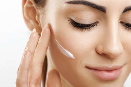 facial care. Female Applying Cream.Portrait Of Young Woman With Cosmetic Cream On Skin. Closeup Of Beautiful Girl With Beauty Product On Soft Skin, Natural Makeup Touching Face. high resolutionの写真素材