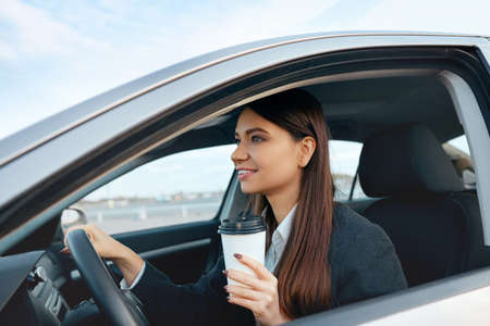 Happy young woman with coffee to go driving her carの写真素材