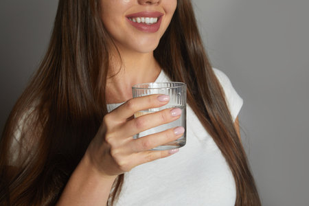 Close up smiling young woman holding glass of clean mineral water, happy beautiful female recommending drinking water.の写真素材