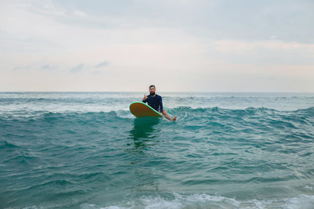 hipster surfer sitting on his surfboard into the ocean water and waiting for a big wave.の写真素材
