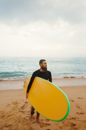 Young male surfer with a surfboard is enjoying a view while walking a sandy beach at sea. Summer, vacation, oceanの写真素材