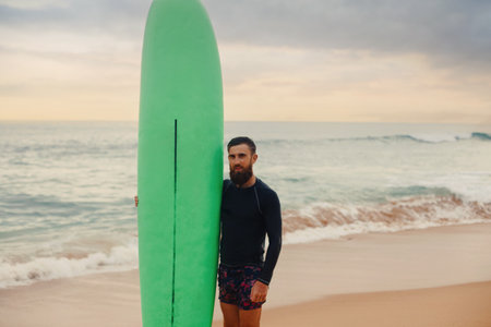 Surfer holding surf board on the beach at sunset. Happy man guy having fun doing extreme sportの写真素材