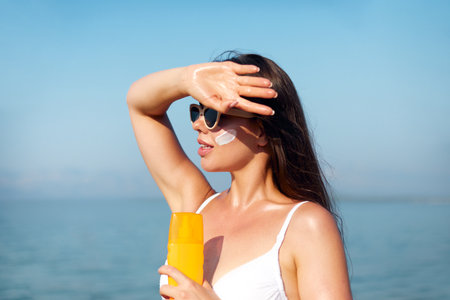 Beautiful Woman Face Portrait Beauty Skin Care Concept. Suncream. Suntan Lotion Beautiful Woman Applying on beautiful on Face. Sunscreen Solar Cream. Sun protection.The Girl Uses Moisturizer Sunblockの写真素材