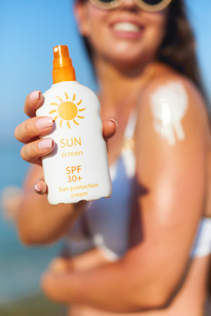 Woman holding sunscreen bottle on the beach and applying moisturizing lotion on skin. Skin care. Sun protection. Suntan. Bottle Sun Creamの写真素材