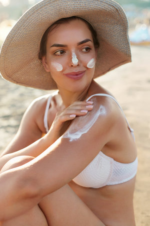 Beautiful Woman in Bikini Applying Sun Cream on Tanned Shoulder. Sun Protection. Skin and Body Care. Girl Using Sunscreen to Skin. Portrait Of Female Holding Suntan Lotion and Moisturizing Sunblock.の写真素材