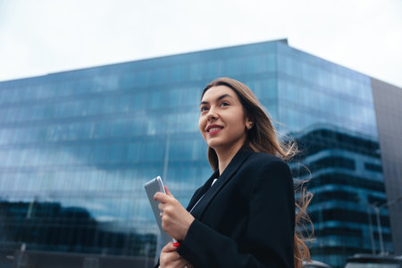 Young woman confidently walks in an urban setting, with modern architecture in the background reflecting a professional lifestyleの写真素材