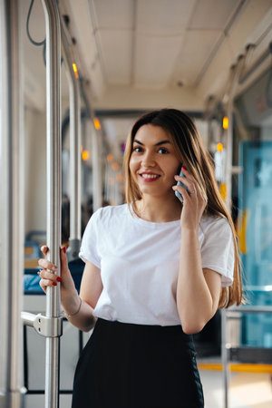 Young woman engaged in a phone conversation while standing in public transport, displaying a...
