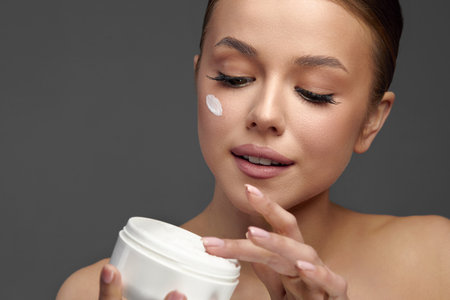 Beauty Woman Concept. Skin care. Young model with Soft skin holding cosmetic cream. Portrait of a female applying moisturizing cream and touching her own face. Skin Protectionの写真素材