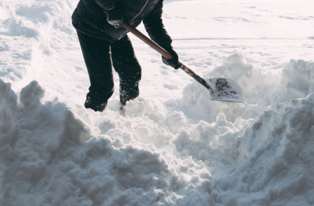 A person is shoveling snow in a residential driveway, surrounded by deep piles of white snow during a winter day. The scene shows a focused effort to clear the path.の素材