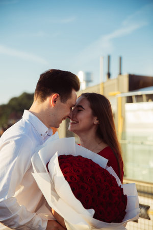Two people hold a large bouquet of roses while smiling and leaning in for a close moment during...