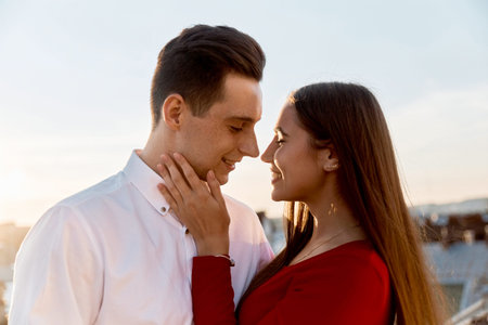 Two people smile at each other during sunset in an outdoor space with a city skyline behind them....