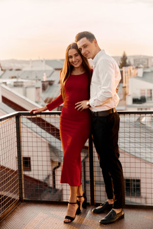 A couple stands on a balcony in a city during sunset, smiling and enjoying the view together. Their close bond is clear.の写真素材