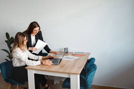 Two women collaborated at a table in an office, working on a laptop and sharing documents during...