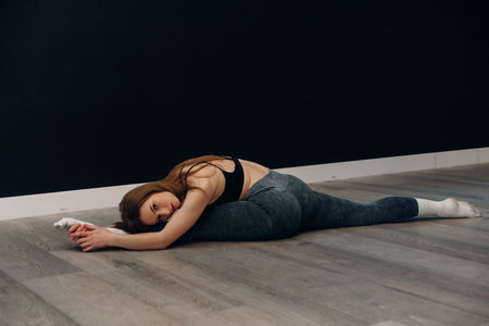 Young female practices stretching in activewear on the floor. She enjoys fitness and promotes a...