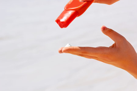 Female hand applying sun protection lotion on the beach, closeup
