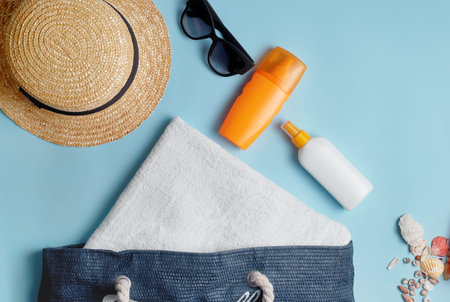 beach bag with beach accessories on a colored background top view. Sunscreen, towel, glasses, hat.