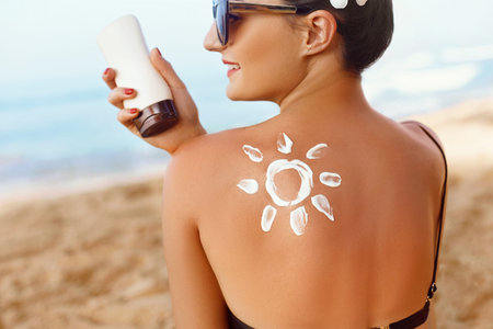 Sun protection. Side view of beautiful young woman applying sun protection cream on her back while...