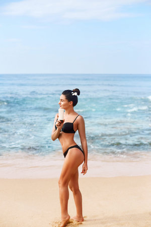 Young Woman in Bikini Holding Bottles of Sunscreen in Her Hands. Skincare. A Female Applying Sun Cream. Using Sun protection. Girl smear moisturizing lotion on skin. Suntanの写真素材