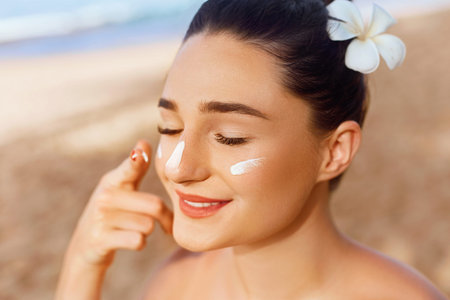 Skin care. Beauty Concept. Young pretty woman applying sun cream and touching her own face. Female...
