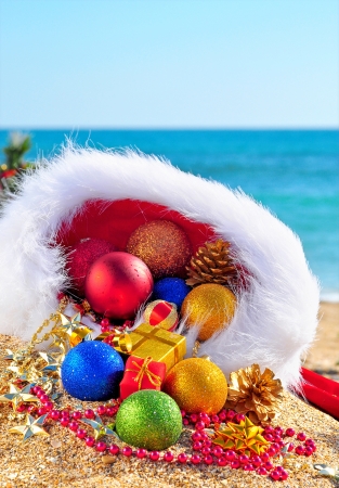 Christmas baubles and gift boxes in the christmas hat on the sand in the seashoreの写真素材