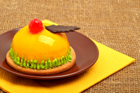 Christmas delicious yellow cake with cherry on ceramic saucer on yellow napkin on sacking background