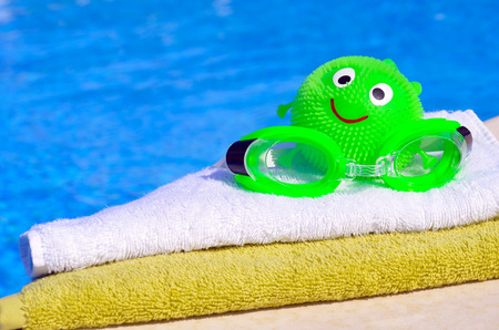 Bath towels, goggles, toy against blue water in the swimming poolの写真素材