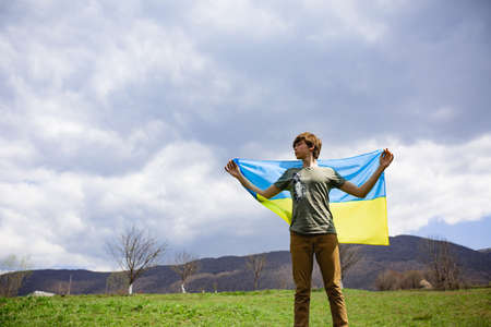 A man holds the Ukrainian flag . Stop war. Against the backdrop of mountains.の写真素材